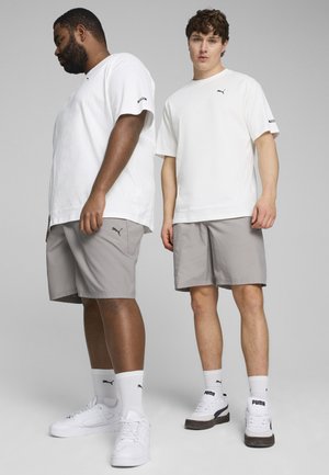 Camisetas de manga corta blancas, pantalones cortos grises y zapatillas blancas con acentos negros. Las camisetas presentan el logo de PUMA en el pecho y las mangas.