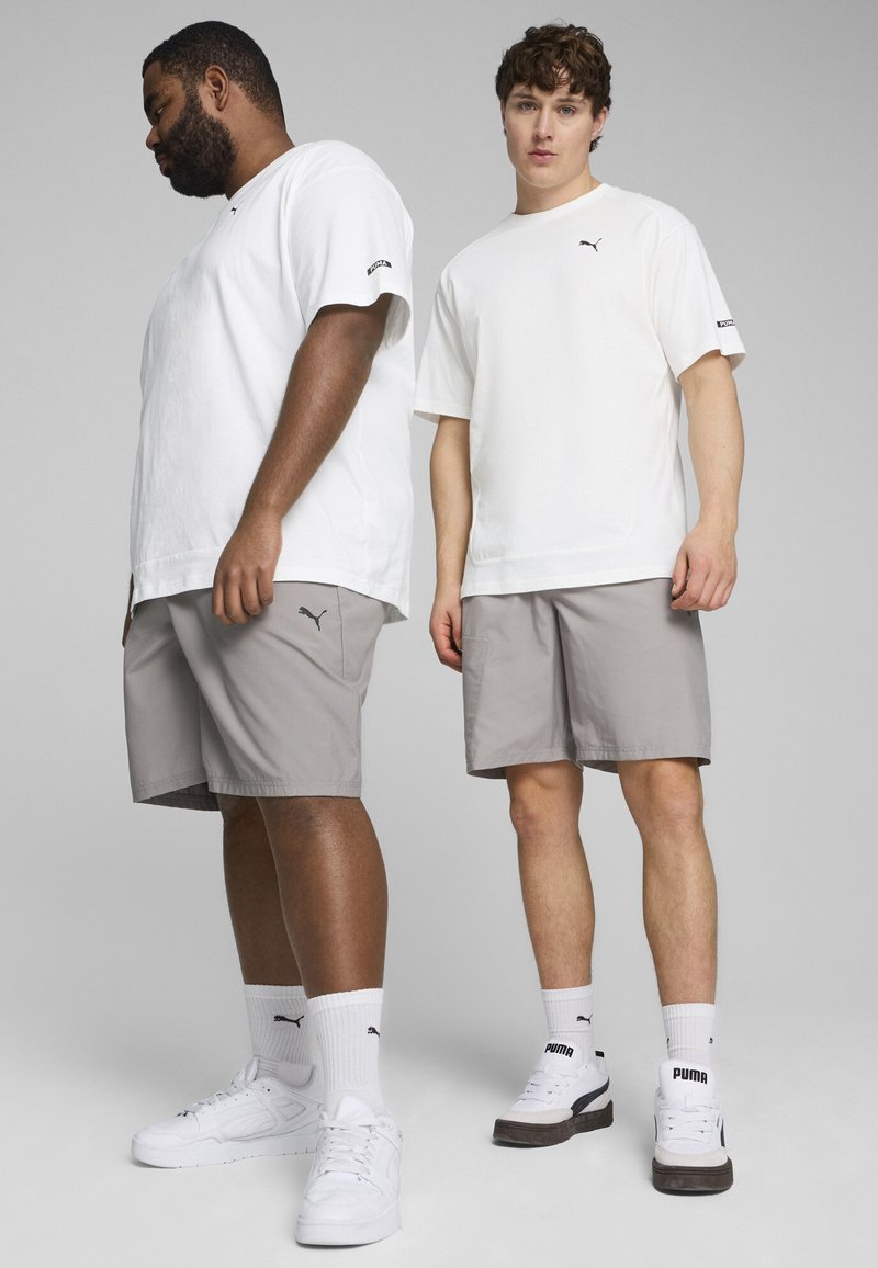Camisetas de manga corta blancas, pantalones cortos grises y zapatillas blancas con acentos negros. Las camisetas presentan el logo de PUMA en el pecho y las mangas.