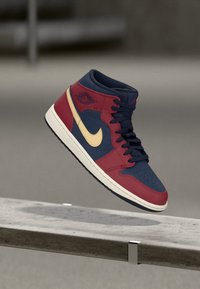 Hochschuhsneaker mit rotem und marineblauem Obermaterial, goldenem Swoosh, perforiertem blauen Zehenbereich, schwarzen Schnürsenkeln und einer weißen Mittelsohle. Klassisches Basketball-Design.