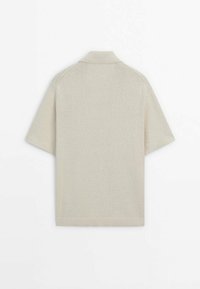 Beige lyhythihainen polo-paita, joka on valmistettu teksturoidusta neulekankaasta ja jossa on tavanomainen kaulus sekä ribattu reunus hihoissa ja helman kohdalla.
