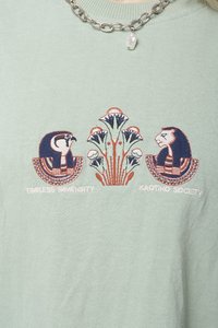 Tricou din bumbac verde deschis, cu designuri brodate reprezentând o bufniță și un leu, însoțite de modele florale, cu textul "Imensitate Timpurie" și "Societatea Kaotiko".