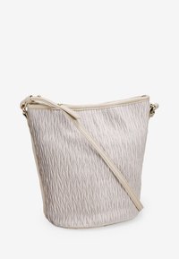 Bolso tipo bucket en material texturizado color crema con diseño plisado, una sola correa de hombro ajustable y acentos en tono dorado.