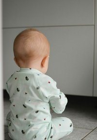 Ljust grönt babydress med mönster av bin och fjärilar, sömlös design och mjuk textur, på ett barn som sitter på ett kaklat golv.