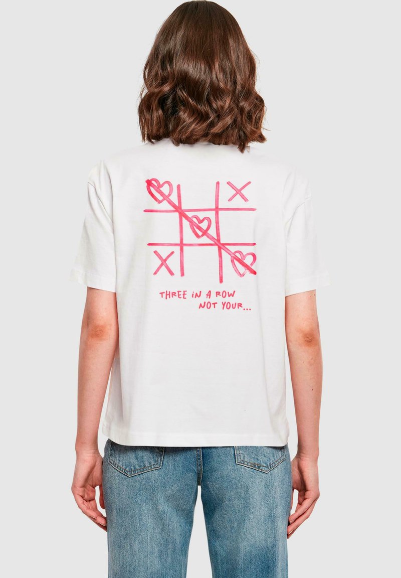 Maglietta bianca in cotone a maniche corte, con una grafica di tris rosa e la scritta "TRE IN FILA NON IL TUO..." sul retro.
