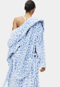 Accappatoio in pile di colore azzurro chiaro con motivo a stampa leopardata. Maniche lunghe, chiusura con cintura, texture morbida e design ampio.