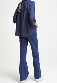 Camicia di denim con maniche a tre quarti, colore blu scuro, orlo leggermente curvato. Abbinata a jeans a zampa d'elefante blu scuro e sneakers bianche.