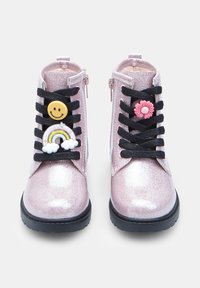 Stivaletti alla caviglia rosa glitter con lacci neri, decorati con charm a forma di sorriso e fiore, suole nere robuste e chiusura con zip sul lato.