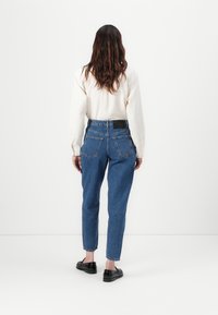 Vaqueros de mezclilla azul de cintura alta con pierna ajustada, cinco bolsillos y un patrón de costura clásico, combinados con una camisa de manga larga de color claro.