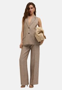 Beige, gestreifter, ärmelloser Anzug mit tiefem Ausschnitt, ausgestattet mit einer Zwei-Knopf-Verschluss, weit geschnittenen Hosen und einer flauschigen cremefarbenen Handtasche.