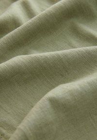 Lysegrønt linnedstof med en blød tekstur, der viser blide folder og en let glans, hvilket fremhæver dets naturlige fibre og farvevariation.