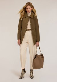 Giacca di jeans khaki con colletto, dolcevita crema, pantaloni beige a vita alta e stivali alla caviglia con stampa serpente. Borsa marrone.