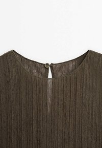 Pronssinvärinen paita, jossa on ribbitekstuuri, pyöreä kaula-aukko, avainreiän takakappale ja yksi nappikiinnitys.