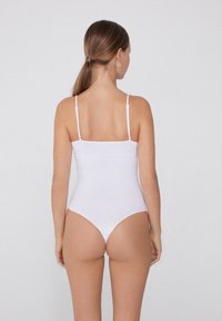 Bílé žebrované body s tenkými nastavitelnými ramínky a vysokým střihem nohavic. Hladký materiál a minimalistický design s obdélníkovým výstřihem na zádech.