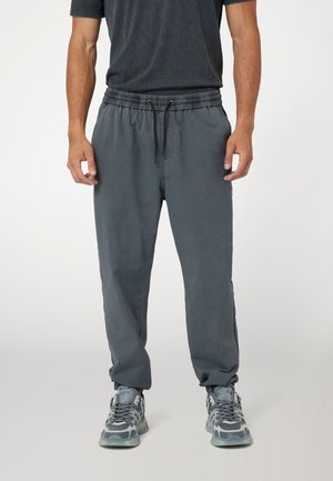 Grå sweatpants med elastisk talje og snor. Stoffet er blødt, har en afslappet pasform og brede manchetter, og de er parret med mønstrede sneakers.