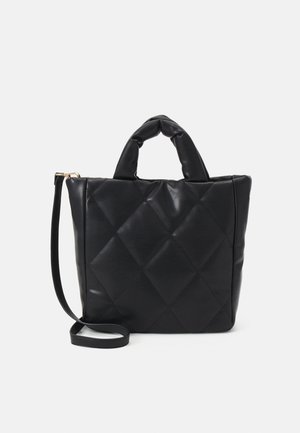 Sac à main en cuir matelassé noir avec des poignées courtes rembourrées et une longue bandoulière réglable sur fond blanc.