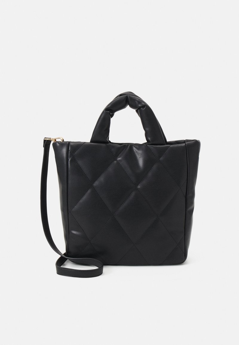 Sac à main en cuir matelassé noir avec des poignées courtes rembourrées et une longue bandoulière réglable sur fond blanc.