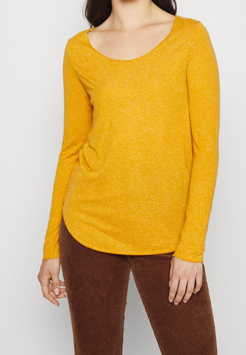 Långärmad t-shirt med rundad halsringning i senapsgul färg, tillverkad av textil med en subtil melerad mönstring, kombinerad med bruna manchesterbyxor.