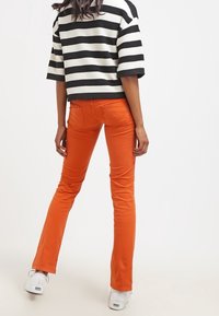 Oranga slim jeans med en lätt utsvängd botten, buren med en överdimensionerad topp i svart och vitt randig och vita sneakers.