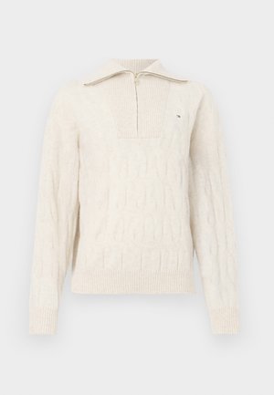 Kremfarget kabelstrikket genser med lange ermer, halv glidelås krage, ribbede mansjetter og nederkant, samt en liten brodert logo på venstre bryst.