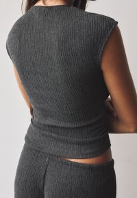 Top sans manches côtelé gris foncé affichant un design ajusté avec un tissu texturé, mettant en avant un col haut et une coupe à la taille.