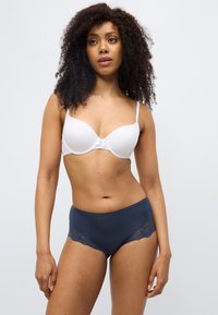 Λευκό μαλακό σουτιέν με ρυθμιζόμενους ιμάντες και λεπτομέρεια φιόγκου. Σκούρο μπλε σλιπ υψηλής μέσης με δαντέλα και υφή λείας υφής.