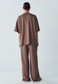 Brown oversized top and wide-leg pants made of soft, textured fabric. Features short sleeves and a relaxed fit with minimal stitching detail.