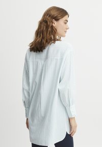 Camicia a maniche lunghe a righe blu chiaro e bianco, con una vestibilità comoda, polsini con bottoni e dettaglio sullo sprone posteriore. Materiale in cotone morbido.