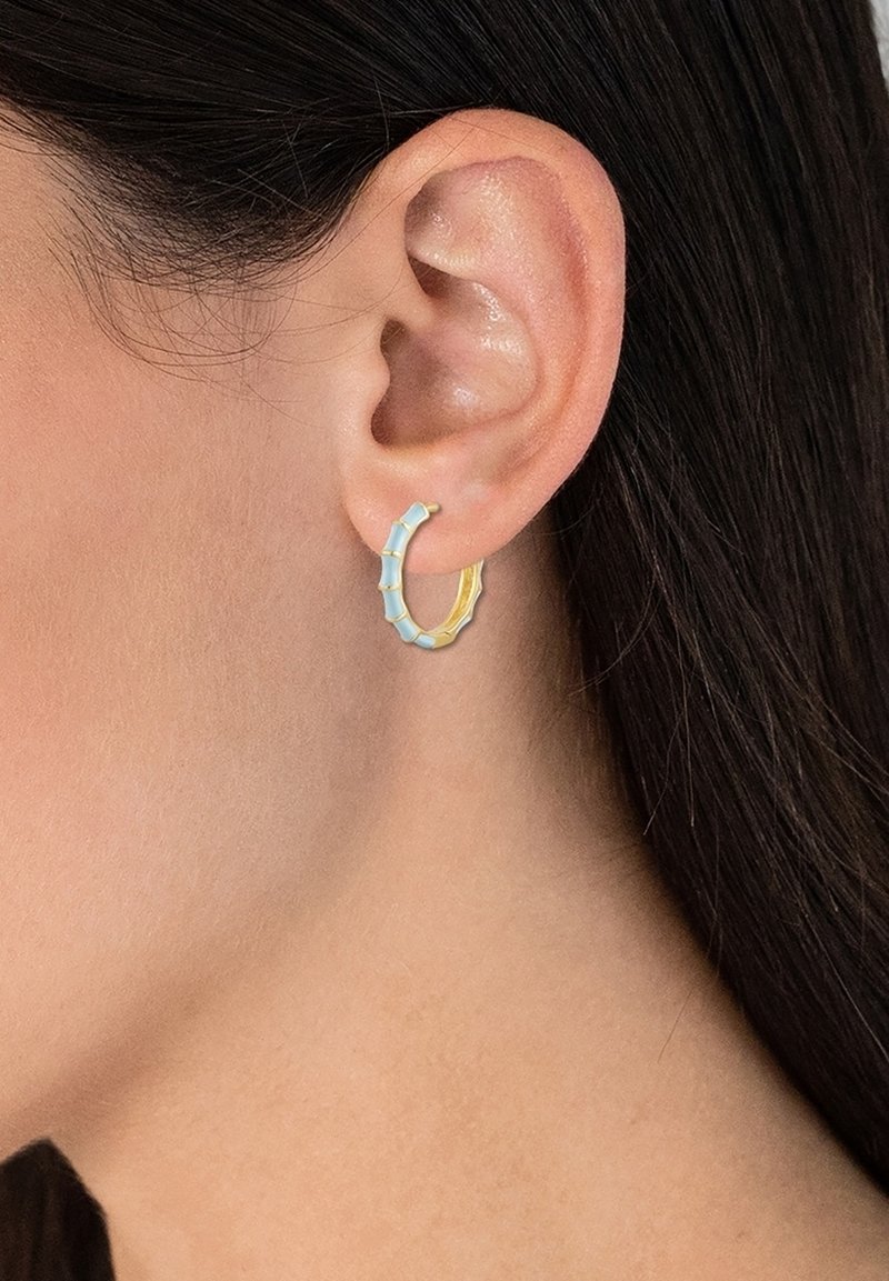Boucles d'oreilles créoles au design en bambou, présentant des couleurs alternées bleu clair et or, avec des surfaces texturées et une forme arrondie.