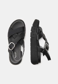 Black leather sandals featuring crossed straps, a silver buckle accent, and a thick, textured sole for stability and grip.