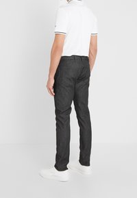 Tmavě šedé slim-fit kalhoty s jemnou texturou, spárované s bílým polo tričkem s černým límečkem a akcenty na rukávech. Bílé sneakers doplňují celý outfit.