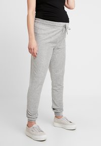 Grå sweatpants tillverkade av mjukt material, med ett elastiskt midjeband och snörning samt slim-fit ben, ihop med vita sneakers.