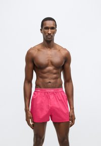 Ροζ αντρικό μαγιό κατασκευασμένο από ελαφρύ ύφασμα, με ελαστική μέση και λογότυπο Calvin Klein. Ομαλή υφή, μήκος μέχρι το γόνατο.