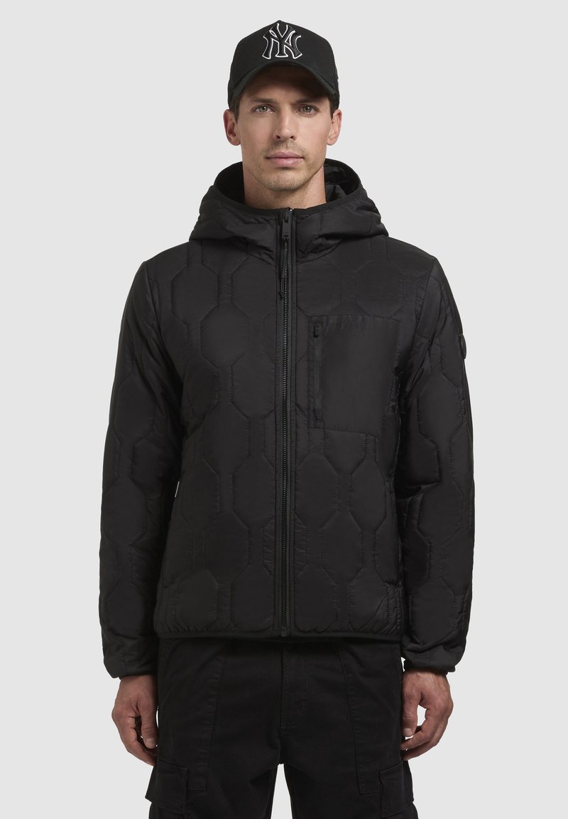 Schwarze Daunenjacke mit hexagonalen Polstern, Reißverschluss und abnehmbarem Kapuzen. Verfügt über eine Brusttasche und strapazierfähigen Stoff. Begleitet von einer schwarzen Mütze.