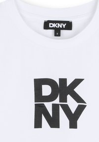 Biała bawełniana koszulka z dużym czarnym logo "DKNY" w pogrubionej czcionce na środku. Metka widoczna na linii szyi.