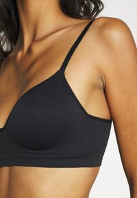 Black seamless bralette featuring thin straps, a smooth texture, and a triangular design. No padding or underwire, with a wide underband.