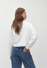Camicia bianca a maniche lunghe con vestibilità rilassata, caratterizzata da un colletto classico e polsini con bottoni, abbinata a jeans in denim blu a vita alta.
