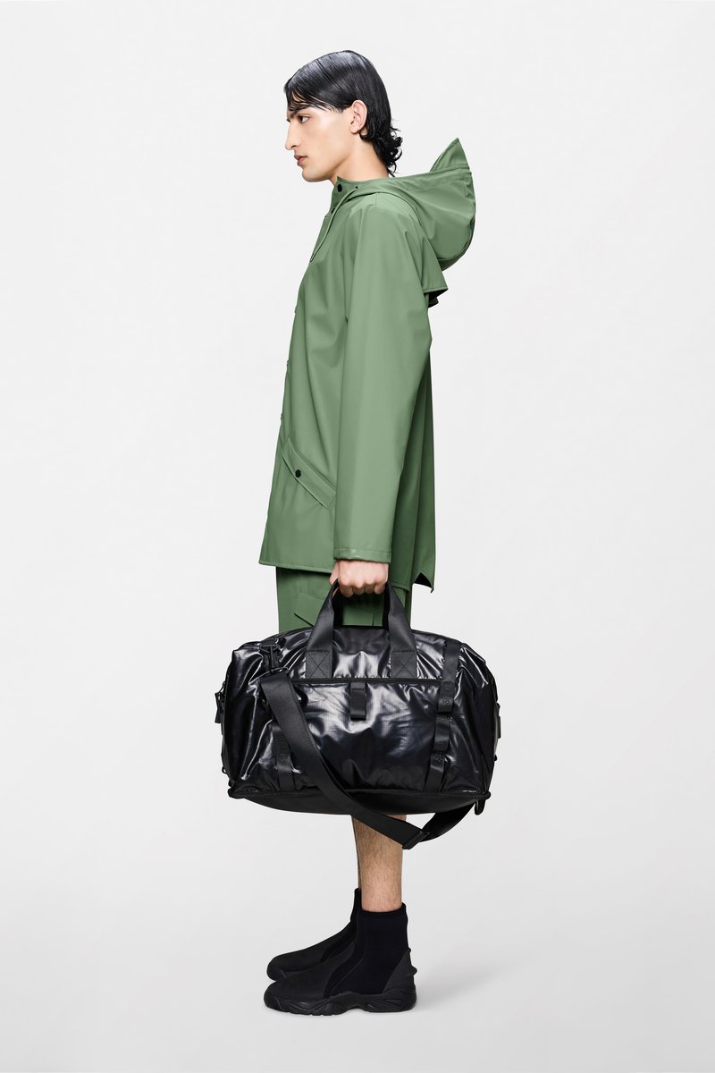 Zelena vodootporna jakna s kapuljačom, uparena s crnom sjajnom torbom s držačem i crnim obućama na navlačenje. Jednostavan dizajn i utilitarističke značajke.