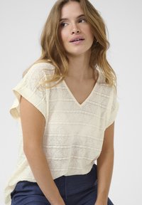 Blusa gialla chiara a maniche corte con scollatura a V, caratterizzata da un tessuto testurizzato con righe orizzontali e una vestibilità rilassata. Abbinata a pantaloni blu scuro.