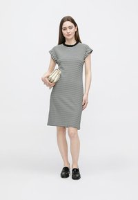 Zwart-wit gestreepte jurk met korte mouwen, ronde hals, knielange snit, gecombineerd met een beige clutch en zwarte loafers.