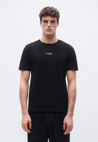 Μαύρο βαμβακερό κοντομάνικο μπλουζάκι με στρογγυλή λαιμόκοψη, με μικρό λευκό λογότυπο "BOSS" τυπωμένο στο στήθος. Απλό σχέδιο, ελάχιστη υφή.