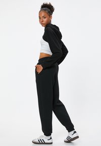 Sort hættekart med en cropped hvid skjorte, parret med sorte sweatpants. Har elastiske manchetter og lommer. Skoene er hvide med sorte accenter.