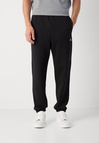 Sorte sweatpants med elastisk talje, sidelommer og et lille hvidt logo på venstre lår. Sammen med hvide sneakers.