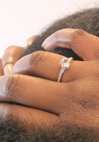 Anello in argento con una pietra centrale rotonda circondata da pietre più piccole; montato su una fascia texturizzata; mani unite.