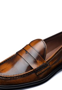 Brown leather loafer with a smooth finish, decorative strap across the front, and visible stitching along the edge.