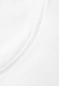 Tissu en coton blanc avec une vue rapprochée d'un col côtelé et de coutures plates. La texture semble lisse et douce.