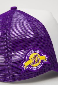 Căciulă de baseball din plasă purpurie cu panou frontal alb, având un patch cu logo care spune "17 TITLURI NBA" în galben și purpuriu.