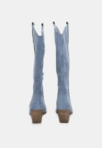 Blå cowboystövlar i mocka med klack, med spetsig tå och utskurna detaljer upptill som designinslag.