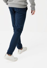 Chino bleu marine en coton, coupe slim avec poches latérales, associés à des baskets blanches avec des accents beiges et des semelles texturées.
