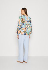 Blusa floreale in colori pastello, con maniche a palloncino e scollatura rotonda. Abbinata a pantaloni larghi blu chiaro e ballerine color nude.