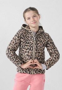 Donsjack met een luipaardprint in beige en zwart, ritssluiting en capuchon. Model draagt roze broek en vormt een hartje met de handen.